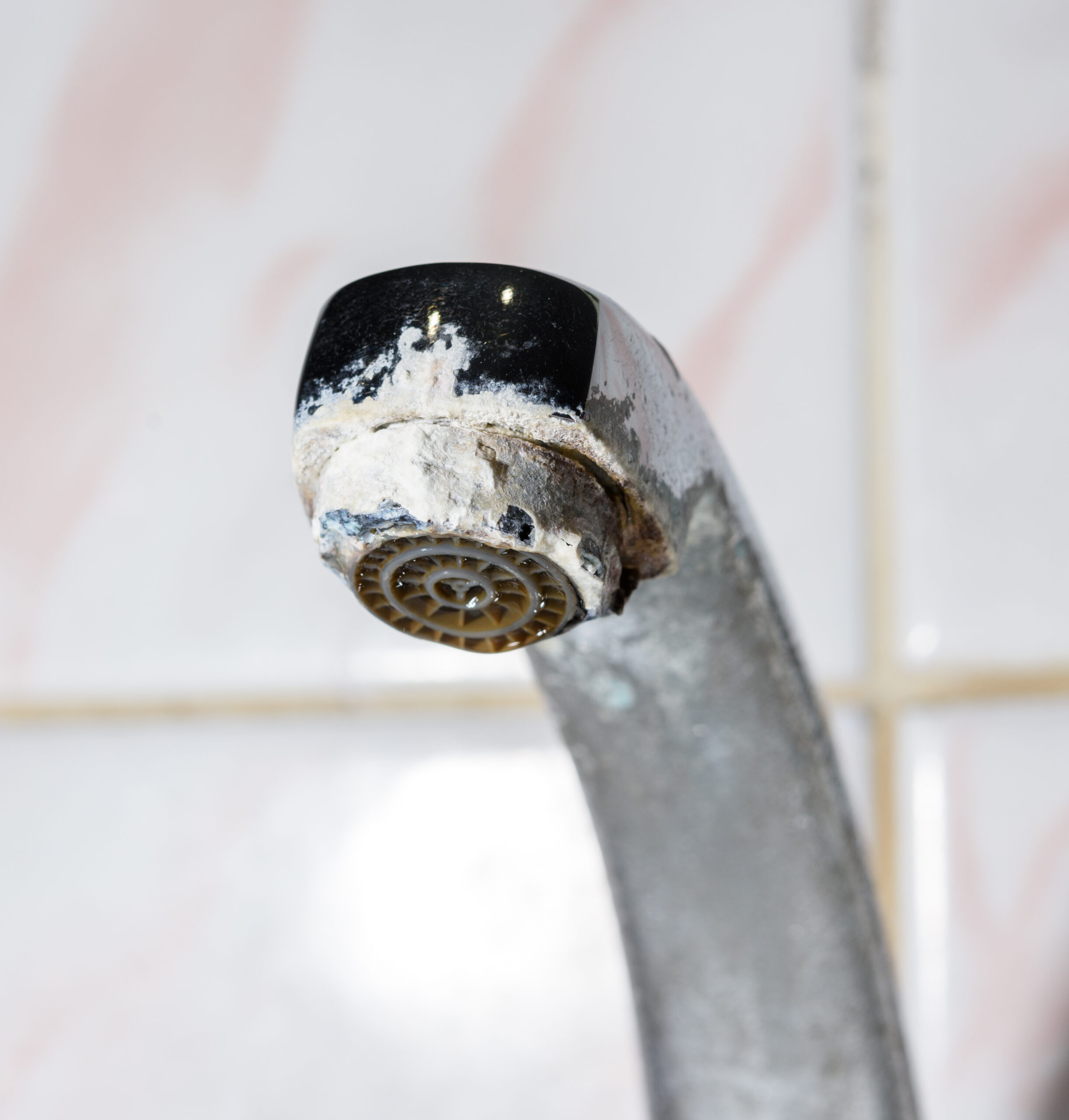 Bathroom faucet showing severe hard water mineral deposits and calcium scale buildup on aerator